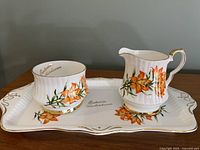 Cream and sugar set with rectangular tray decorated with orange Prairie Lily flowers and gold trim.