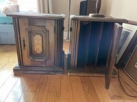 Pair of wooden end tables with cabinet doors open and closed, showing carved wooden panels and multiple vertical internal divider slots for storage.