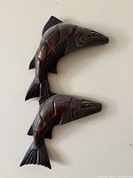 Front view of two dark wood carved fish wall decorations with geometric patterns hung on wall.