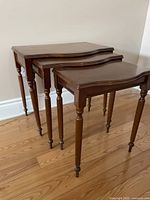Photo showing three solid wood nesting tables of decreasing size, each with carved legs and smooth rectangular tops, nested inside each other on a hardwood floor.