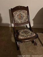 Full front view of the antique folding rocking chair showing the floral upholstered seat and backrest with carved wooden frame.
