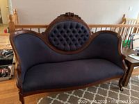 Front view of antique settee sofa showing detailed carved wooden frame, blue tufted upholstery on backrest, and curved armrests.