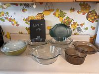Photo of three clear Anchor Hocking glass casserole dishes (two without lids, one with lid), green Mirenex bowl with lid, and two brown glass bowls with bevelled pattern made in Brazil, all displayed on kitchen counter with vintage wallpaper.