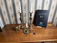 Lot showing all items: two tall brass candle holders with white taper candles, small brass candle holder with candle, brass elephant figurine, metal bottle opener with blue detail