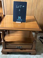 Full view of the wooden side table showing the drawer with ornate handle, shelf, and turned legs