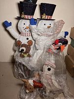 Photo showing two tall white glittery snowmen wearing black glitter top hats with holly, and animal figures wrapped in plastic, including a bear and a penguin.