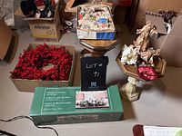 Photo showing a box with a large red berry wreath, three angel figurines on wooden pedestals, a holiday centerpiece in a green box, and other Christmas decorations packed into boxes.