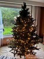 Full view of artificial Christmas tree illuminated with some lights showing turnover in brightness, some bulbs appear to be burnt out.