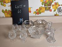 Overview of set with six mini pinwheel crystal glasses, footed candy dish, two taper candle holders and two Ashtrays on kitchen counter with floral wallpaper background.