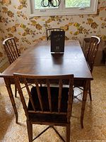 Back view of wooden dining table and spindle back chairs showing details of chair design and table surface.