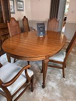 Dining table and six cane back chairs in a beige carpeted room with wallpaper, showing table without leaf and chairs around.