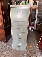 Full frontal view of the 4-drawer metal filing cabinet showing its light gray color, drawer handles, and label holders.