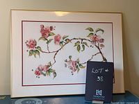 Framed floral print showing a branch with pink and cream flowers and green leaves, framed in a slim gold frame.