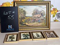 Photo showing the framed landscape painting with a cottage, set in gold-tone frame, alongside four small framed Hummel prints depicting traditional German child figurines.