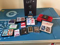 Top down view on a blue game table showing all playing card decks with a red automatic card shuffler and two novelty photo decks