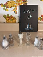 Front view of three sets of salt and pepper shakers on a counter with a blackboard in background