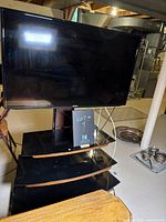 Black Samsung LED TV on stand with three glass shelves shown from front angle in basement setting.