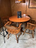 Round wooden dining table with four matching traditional style chairs arranged around it, light brown finish, showing minor wear and scratches on table surface.