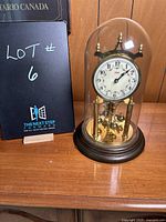Front view of the vintage anniversary clock under a glass dome with wooden base, showing the clock face and surrounding brass details.
