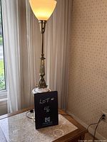Full view of the vintage Stiffel table lamp placed on a side table near window, showing entire lamp with base, pole, and frosted glass shade, turned on.
