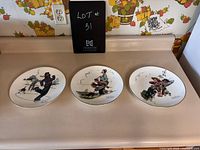 Three Norman Rockwell collectible plates shown from front on a kitchen counter, each plate depicting a different scene and measuring about 10 3/4 inches diameter.