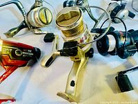 Photo showing 5 spinning fishing reels with silver and gold finishes, some with visible wear and paint chips on metal surfaces.