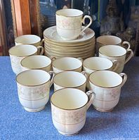 Front view of 12 teacups arranged with saucers stacked behind on blue surface.