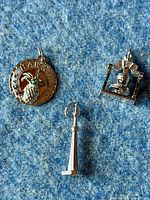 Three 925 sterling silver charms laid side by side on a blue fabric background, showing the Hawaii charm with gem-set pineapple, Liberty Bell charm, and CN Tower charm.
