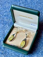 Pair of teardrop-shaped drop earrings with oval green Connemara Marble stones in silver settings inside an original green and cream Connemara Marble box, showing brand name inside lid and price tag.