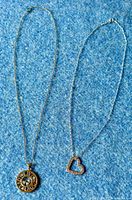 Two 925 sterling silver necklaces laid flat on blue fabric background, showing pendants and chains.