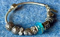 Side view of the Pandora bracelet with various sterling silver charms including a blue glass charm and engraved charms.