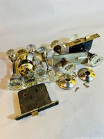 Overview of multiple antique door knob sets showing clear glass knobs, brass backplates, and metal lock plates with screws.