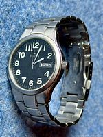 Front angled view of the Bulova watch showing the black dial, white numerals, and day-date window.