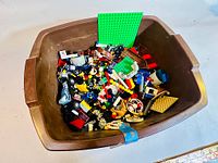 Brown container filled with assorted Lego pieces and green base plates.