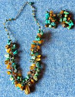 Full view of necklace and earrings set on blue felt background, showing clusters of amber, turquoise and tiger's eye stones.