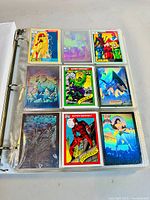 Photo shows a binder page with 9 collectible cards, including holographic cards featuring Firestar, Hulk, Batman, Daredevil, Wonder Woman, and others.