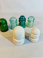 Full set of four threaded glass insulators in blue and green tones with two white porcelain insulators in front.