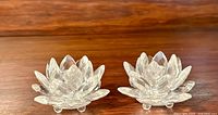 Pair of clear cut crystal candlesticks shaped like water lily lotus flowers on wood surface, shows design and shape.