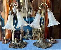 Pair of Tiffany style tulip lamps with frosted glass shades on bronzed lily pad bases shown side by side on blue surface.