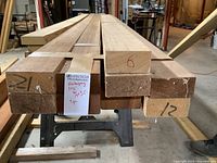 Oblique overhead view of stacked mahogany boards on sawhorse showing ends marked with numbers and a label.