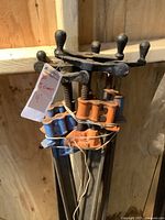 Bundle of five 4ft bar clamps shown upright, tied together with string. Orange and blue cast iron clamp heads visible, with black rounded screw handles.