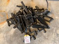 Photo showing a pile of eight black metal clamps bundled together with wire on a concrete floor.