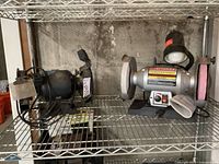 Two bench grinders on metal shelving: black Ohio Forge 6-inch grinder and silver Craftsman 8-inch variable speed grinder with work light.