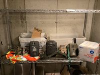 Shelving with 6 trail cameras in different models and colors along with orange hi-vis vest and some mounting accessories