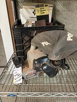 Overall view of Porter Cable sander on metal shelving with sanding supplies including belts and 3M sandpaper sheets behind it.