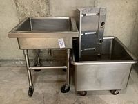 Full view of cleaning station showing stainless steel sink on caster stand and large tub with caster wheels and handle