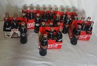 Six-packs of Coca-Cola glass bottles in red cardboard carriers, showing unopened bottles with sports-themed labels including Phoenix Coyotes