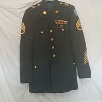 Full view of the Army full dress uniform jacket showing buttons, chevrons, patches, and medals on fabric.