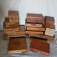 Overview of all 14 wooden cigar boxes stacked and arranged together showing various sizes, finishes, and brands.