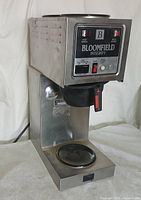 Full front side view of the stainless steel Bloomfield Integrity coffee maker showing the control panel, warming plates on top, and the missing pot area below.